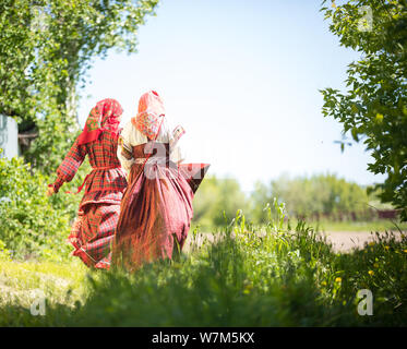 Two young women in traditional russian clothes stand in the field between the trees Stock Photo