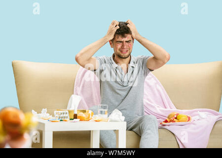Young man suffering from allergy to citrus fruits. Having skin rash, itching, Sneezing in the napkin, sitting surrounded by grapefruits and oranges. Taking medicine with no result. Healthcare concept. Stock Photo