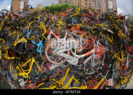 Abandoned bicycles of Mobike (orange), ofo (yellow), Xiaoming Danche, or Xiaoming Bike (blue), and other Chinese bike-sharing services are piled up at Stock Photo