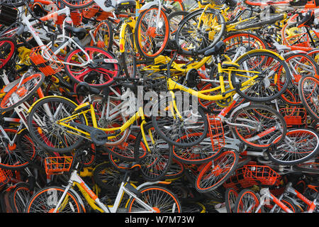 Abandoned bicycles of Mobike (orange), ofo (yellow), Xiaoming Danche, or Xiaoming Bike (blue), and other Chinese bike-sharing services are piled up at Stock Photo