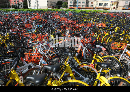 Abandoned bicycles of Mobike (orange), ofo (yellow), Xiaoming Danche, or Xiaoming Bike (blue), and other Chinese bike-sharing services are piled up at Stock Photo