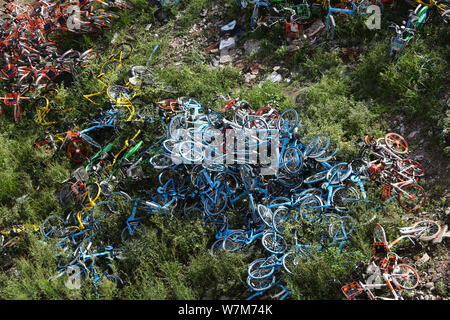 Abandoned bicycles of Mobike (orange), ofo (yellow), Xiaoming Danche, or Xiaoming Bike (blue), and other Chinese bike-sharing services are piled up at Stock Photo