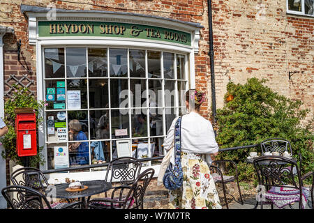 A young lady dressed up in a 1940s style flowery dress looking in the window of the tea shop in the quiet village of Heydon in Norfolk Stock Photo