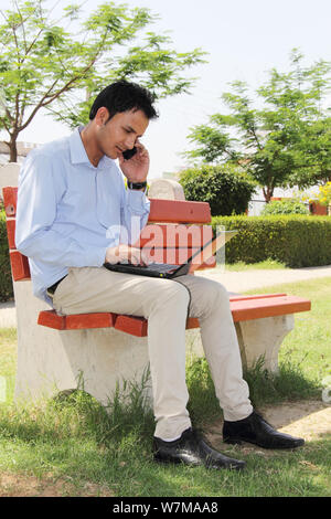 Young man using laptop and mobile phone in a park Stock Photo