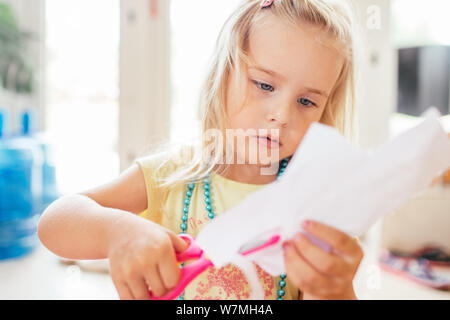 Little blonde girl with scissor at preschool. Education.Portrait of a little Cute baby girl cutting a paper Stock Photo
