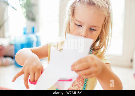 Little blonde girl with scissor at preschool. Education.Portrait of a little Cute baby girl cutting a paper. Stock Photo