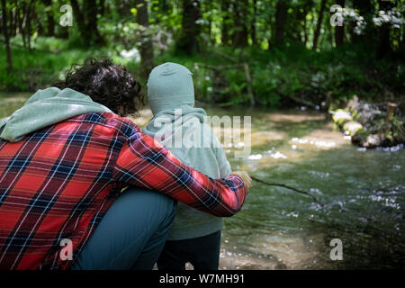 Young dad and toddler girl playing with a wooden stick, near a stream in green woods Stock Photo