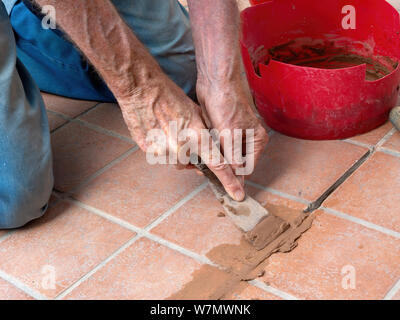 Unidentified man, workman, repairing grout between outdoor terracotta