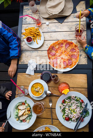 Top view family, adult and children, dinner concept, on wooden table: Eating foods Salad with shrimps, soup with sea food, pizza, salad with chicken, Stock Photo