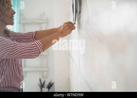 Independence woman working at home repairing things on the white wall in the room - concept of do it yourself work inside house - Stock Photo