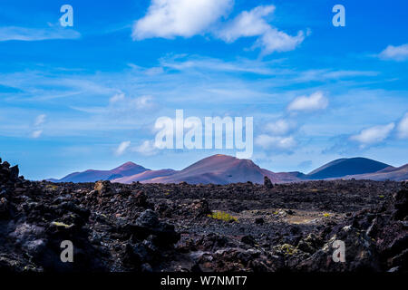 Spain, Lanzarote, Arid black lava fields surrounding red volcanic mounts in timanfaya nature landscape Stock Photo