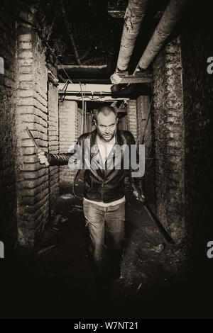 portrait of a serial killer holding knives and running inside an underground tunnel. Stock Photo