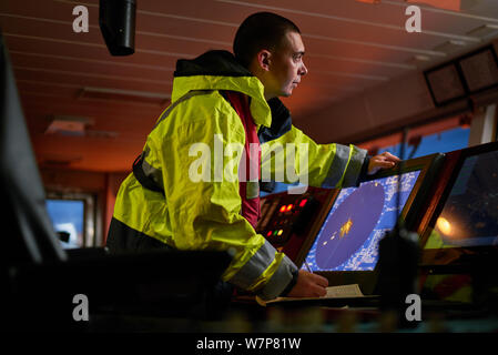 Navigator. pilot, captain as part of ship crew performing daily duties with VHF radio, binoculars, logbook, standing nearby to ECDIS and radar station Stock Photo