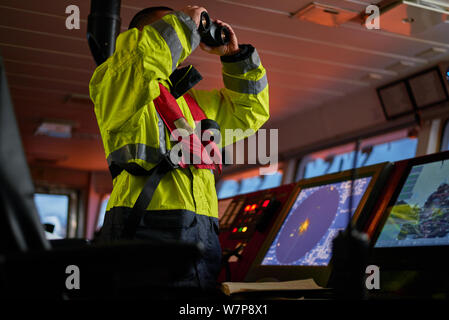 Navigator. pilot, captain as part of ship crew performing daily duties with VHF radio, binoculars, logbook, standing nearby to ECDIS and radar station Stock Photo