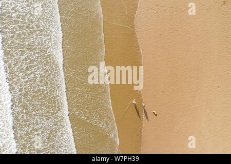 Aerial view of people walking and their shadow on a sand beach next to the waves in Porthcawl Wales UK Stock Photo