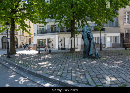 Nantes, France - May 12, 2019: One elderly woman sitting on the bench under green trees near statue of Anne de Bretagne Queen of France. Nantes France Stock Photo