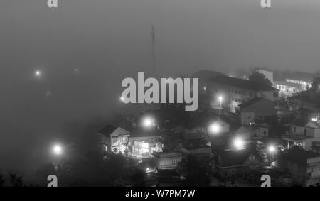 The city sunk in the night fog with bright electric lights in the mist creating a fanciful, impressive scene in Da Lat, Vietnam Stock Photo