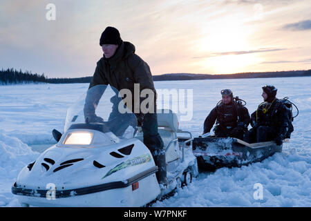 Two divers on a sledge towed by Ski-doo snowmobile to go ice diving, Arctic circle Dive Center, White Sea, Karelia, Northern Russia, March 2010 Stock Photo