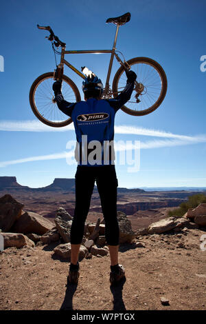 Mountain biker holding up his bike on top of Murphy Climb along the White Rim Road in the Island In The Sky District. Canyonlands National Park, Utah, October 2012. Model released. Stock Photo