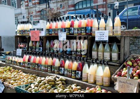 Bottles of organic juice alongside local apples and pears on sale at Marylebone Farmers Market, London, England, UK, March 2009 Stock Photo