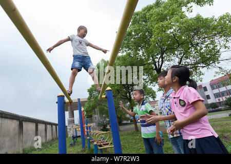 Eight-year-old Chinese boy Yang Shuntao, who was born with blue eyes and diagnosed with a severe hearing loss, plays on parallel bars at his school in Stock Photo