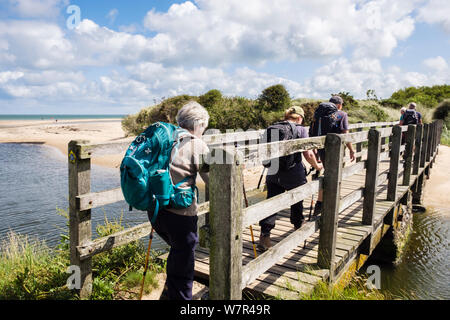 Hikers walking across wooden footbridge over a stream on Wales coastal footpath in summer at Lligwy Bay, Isle of Anglesey (Ynys Mon), Wales, UK Stock Photo