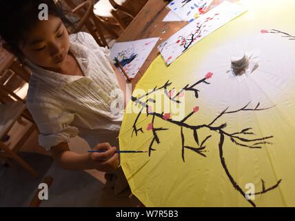 A child paints on an oil paper umbrella at the stuidio of Yu Wanlun, the seventh generation successor of Luzhou's oil paper umbrella, in Hangzhou city Stock Photo