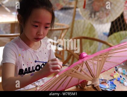 A child paints on an oil paper umbrella at the stuidio of Yu Wanlun, the seventh generation successor of Luzhou's oil paper umbrella, in Hangzhou city Stock Photo