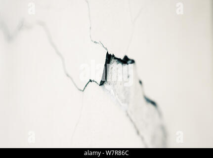 Abstract background depicting a deep curved crack in the plaster on a white smooth wall. Stock Photo