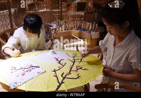 Chinese children paint on an oil paper umbrella at the stuidio of Yu Wanlun, the seventh generation successor of Luzhou's oil paper umbrella, in Hangz Stock Photo