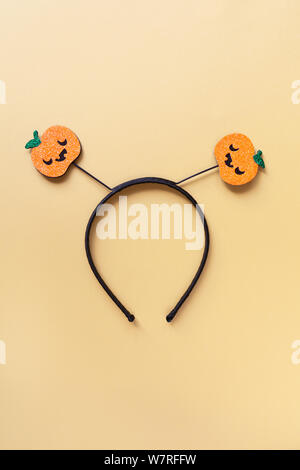 Halloween party accessory, rim with two shiny pumpkins with cute creepy faces. Pastel yellow background, central composition. Holiday flat lay. Minima Stock Photo