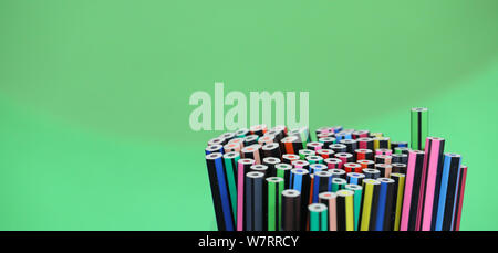 stand of many multi colored bright drawing pencils in a circular arrangement with a plain light green background. Stock Photo