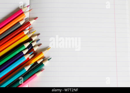 Colored pencils lie on a striped notebook. There is a place for text. Colored pencils are shown in close-up. Soon to school. Draw with pencils in a no Stock Photo