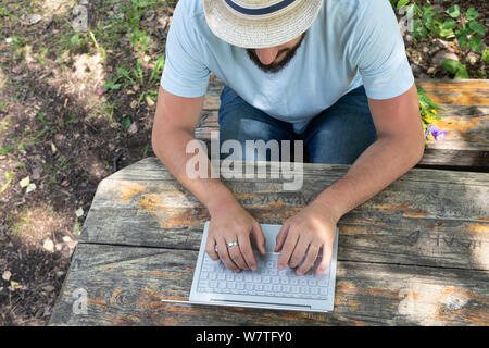 business, education, people communication and technology concept - man in a park on a bench typing on a laptop keyboard Stock Photo