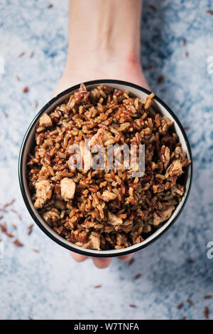 high angle view of the hand of a caucasian man holding a white ceramic bowl with fried red rice with diced chicken meat, on a marbled table or counter Stock Photo