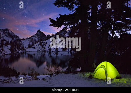 Tent lit up at night after an early winter snowfall, with Kaleetan Peak and Gem Lake, near Snoqualmie Pass, Cascades,  in Washington, USA, October 2013. Stock Photo
