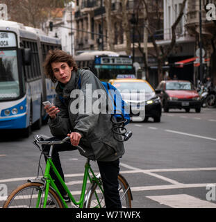 Buenos Aires, Argentina, August 1, 2019. Young man with smartphone on bike in the middle of traffic. Stock Photo