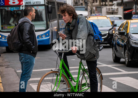 Buenos Aires, Argentina, August 1, 2019. Young man with smartphone on bike in the middle of traffic. Stock Photo