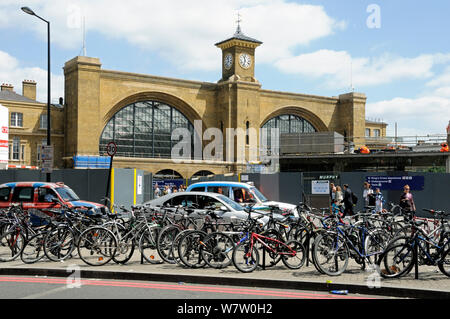 Bicycles attached to bike racks in front of taxis and traffic with King's Cross Station behind, London, England, UK, July 2013. Stock Photo