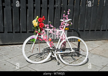 White bike adorned with pink flowers and red and yellow roses, Dalston Junction, London Borough of Hackney, England, UK, May 2013. Stock Photo