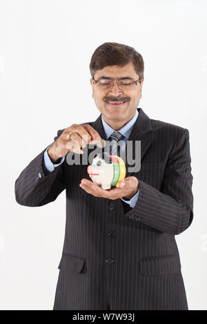 Businessman inserting a coin into a piggy bank Stock Photo