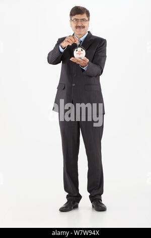 Businessman inserting a coin into a piggy bank Stock Photo