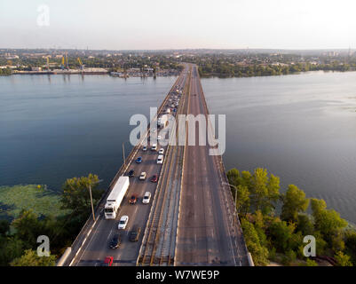 View from the drone to heavy traffic on a bridge over a river with a view of the city in the distance. Stock Photo