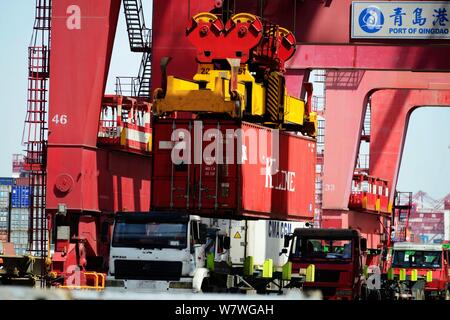 A crane vehicle lifts containers to be shipped abroad from trucks on a quay at the Port of Qingdao in Qingdao city, east China's Shandong province, 13 Stock Photo