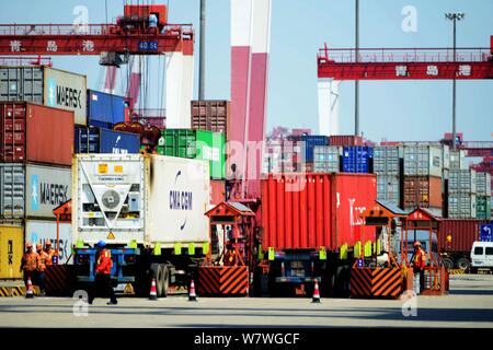 A crane vehicle lifts containers to be shipped abroad from trucks on a quay at the Port of Qingdao in Qingdao city, east China's Shandong province, 13 Stock Photo
