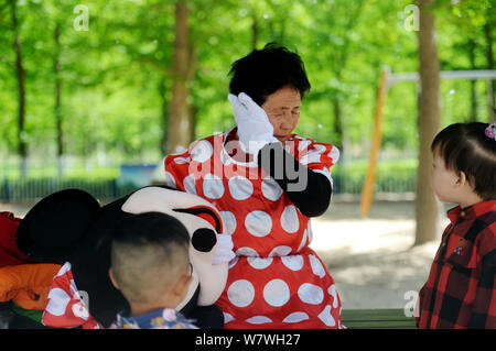 Elderly Chinese woman Yin Pizhi in her 70s, who plays Minnie Mouse to raise money for the treatment of her daughter-in-law, wipes her sweat at a park Stock Photo