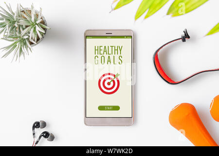 Healthy Goals concept. Fitness healthy goals with mockup mobile phone on white table with dumbbells,smart watch, earphone. Mock up smartphone for fitn Stock Photo