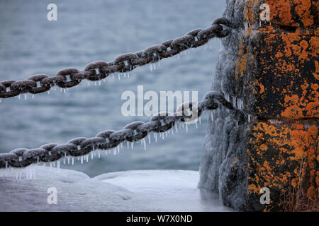 Ice covering old rusty chain & stone barrier, Lake Superior, Gooseberry Falls State Park, Minnesota, December. Stock Photo