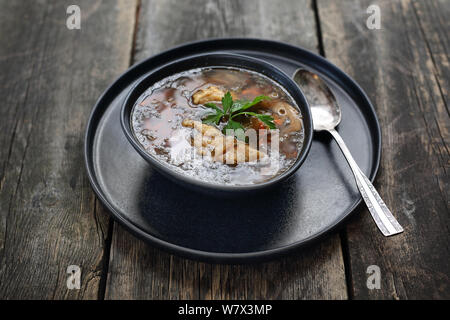 Soup in a black plate on a wooden background. Stock Photo