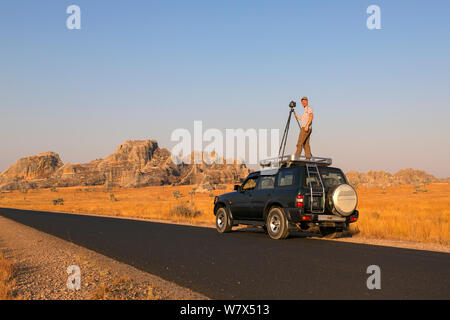 Wildlife photographer Ingo Arndt on assignment for a migrating locust story, standing on roof from 4WD taking pictures. Isalo National Park, Madagascar. August 2013. Stock Photo